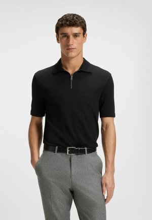 Black polo shirt with a short zipper, soft fabric, and a flat collar, paired with gray patterned trousers and a black belt.