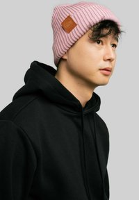 Różowa, prążkowana czapka z dzianiny z skórzaną naszywką, noszona z czarną bluzą z kapturem. Skupienie na fakturze i kontraście kolorów.
