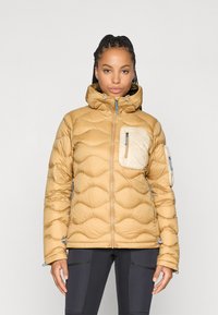 Tan pufferjack met een hoge kraag, gequilte textuur, blauwe ritsen en twee met rits gesloten zakken. Eén zak heeft een contrasterende lichte kleur.