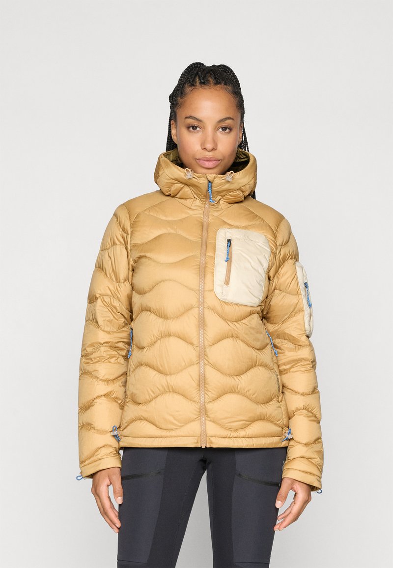Giacca puffer beige con colletto alto, texture trapuntata, cerniere blu e due tasche con zip. Una tasca presenta un colore chiaro a contrasto.