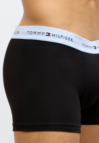 Mustad poksijad sinise vöökohaga, millel on "TOMMY HILFIGER" logo. Sile tekstuur, keha järgiva lõikega ja nähtava õmblusega detailid.