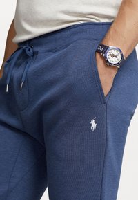 Marina blöja gjord av mjukt tyg, med dragsko i midjan och en liten vit hästlogotyp på vänster lår.