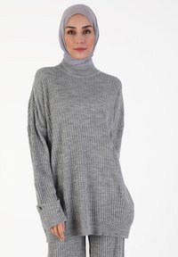 Helles graues, geripptes Sweatshirt mit hohem Kragen und langen Ärmeln. Hat eine lockere Passform und umgeschlagene Bündchen, gefertigt aus weichem, strukturiertem Material.