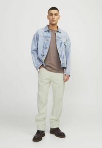 Lyseblå denimjakke over en brun t-shirt, parret med hvide bukser og mørkebrune støvler. Outfit'et har en afslappet pasform og minimal detaljer.