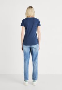 Marineblauwe katoenen t-shirt met een ronde halslijn en korte mouwen, gecombineerd met lichtblauwe spijkerbroek en witte schoenen met groene accenten.