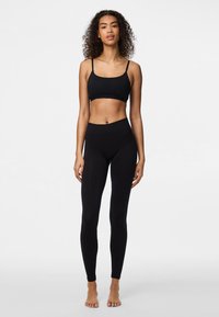 Svart sportbehå och högmidjade leggings, båda i ett smidigt, stretchigt material. Behåna har tunna axelband, och leggingsen har en sömlös design.