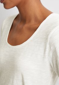 Wit, lichtgewicht t-shirt met een ronde hals en korte mouwen. Zachte textuur en een subtiel, fijn patroon zichtbaar op de stof.