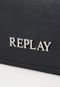 Svart teksturert lærpung med preget sølv "REPLAY"-logo. Har pent søm og en glatt finish. Kompakt rektangulær form.