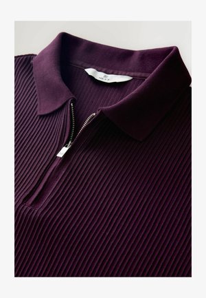 Fioletowa, w paski koszulka polo z zamkiem błyskawicznym przy kołnierzu. Tkanina wydaje się mieć teksturę z pionowymi żebrowaniami. Etykieta marki widoczna wewnątrz kołnierza.