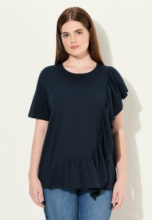 Camiseta azul marino de manga corta, con escote redondo y detalle de volantes asimétricos en el lado, con bajo peplum. Tejido suave.