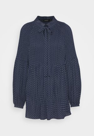 Blouse bleu marine à manches longues avec petits motifs circulaires blancs et un nœud-cravate au col.