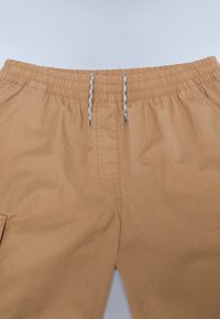 Shorts marron clair avec une taille élastique, dotés d'un cordon de serrage de couleurs contrastées et de poches latérales pour plus de praticité.