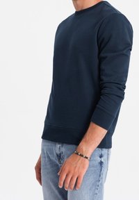 Mörkblå sweatshirt i en mjuk, slät bomullsblandning med rund halsringning och långa ärmar. Ribbad mudd och fåll. Bärs med ljusblå jeans.