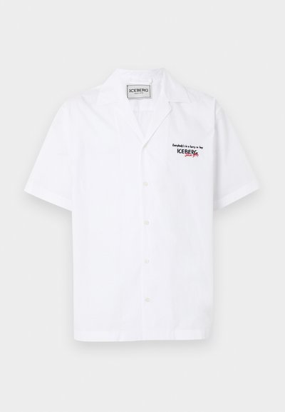 Λευκό πουκάμισο με κοντό μανίκι και κουμπιά, γιακάς τύπου κάμπινγκ, μαύρο και κόκκινο κείμενο "ICEBERG since 1974" στο αριστερό στήθος και ετικέτα της μάρκας στο εσωτερικό του γιακά.