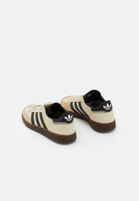 Beige sneakers met zwarte strepen en accenten, leren bovenkant met textuur, rubberen zool en zwart logo op de hiel. Klassiek sportief ontwerp.