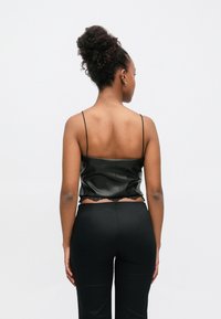 Maiou din piele ecologică neagră cu bretele subțiri, cu dantelă la tiv. Stilizat cu pantaloni negri mulați.