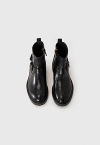 Un par de botines de cuero negro con hebillas laterales y cremalleras interiores sobre un fondo claro y liso, vistos desde arriba.