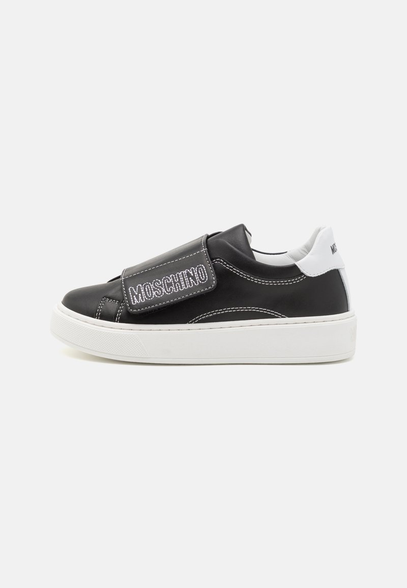 Zapatilla de cuero negra con suela blanca, que presenta una tira de Velcro con el nombre "Moschino" en blanco. Acentos blancos en el talón.
