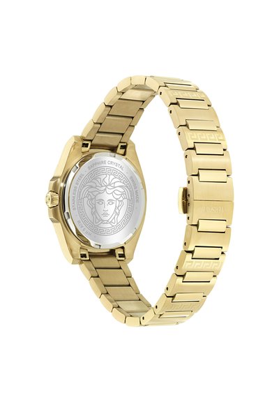 Bracelet de montre en métal doré avec une tête de Méduse gravée sur une plaque arrière argentée, présentant un motif de clé grecque sur les maillons du bracelet.