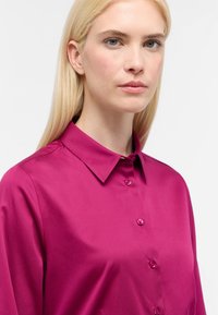 Camicia di seta fucsia con colletto classico, maniche lunghe e chiusura con bottoni. Tessuto morbido con bottoni abbinati.