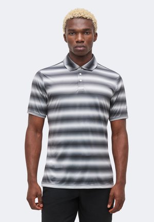 Homme aux cheveux blonds courts portant un polo à manches courtes gris et blanc à rayures horizontales, debout devant un fond uni.