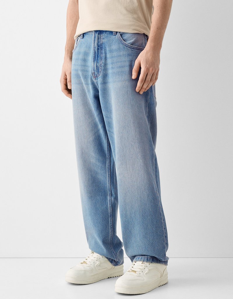 Ausgebleichte hellblaue Jeans aus Denim mit lockerem Schnitt, ausgestattet mit einem Knopf- und Reißverschluss, Fünf-Taschen-Design und geradem Bein. Kombiniert mit weißen Sneakers.