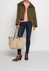 Olivgrön kort jacka med två framfickor, rosa stickad tröja, mörka jeans och beige toteväska med bruna handtag och accent.