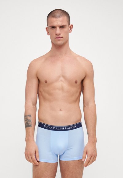 Vaaleansiniset bokserit, jotka on valmistettu pehmeästä kankaasta, ja joissa on tummansininen vyötärönauha, jossa lukee "POLO RALPH LAUREN". Sujuva pinta, istuva muotoilu.