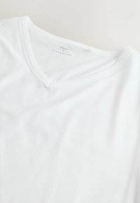 Fehér pamut póló V-nyakkivágással és rövid ujjal, sima tapintású, belső gallérján nyomtatott címkével.