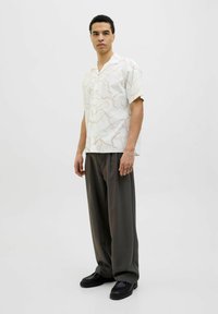 Camisa blanca de manga corta con patrones abstractos en rosa claro, combinada con pantalones grises holgados y zapatos negros. Diseño minimalista.