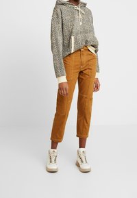 Sudadera corta con capucha y estampado de leopardo en gris y beige, combinada con pantalones de pana marrones que tienen bolsillos y un diseño de pierna recta.