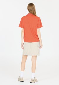 Orange kortärmad polo med en strukturväv, kombinerad med en beige kjol med sidficka, och beige sneakers med vita strumpor.
