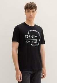 Čierne bavlnené tričko s krátkymi rukávmi a okrúhlym výstrihom, na ktorom sú biele nápisy "DENIM" a "TOM TAILOR" v kruhovom dizajne.