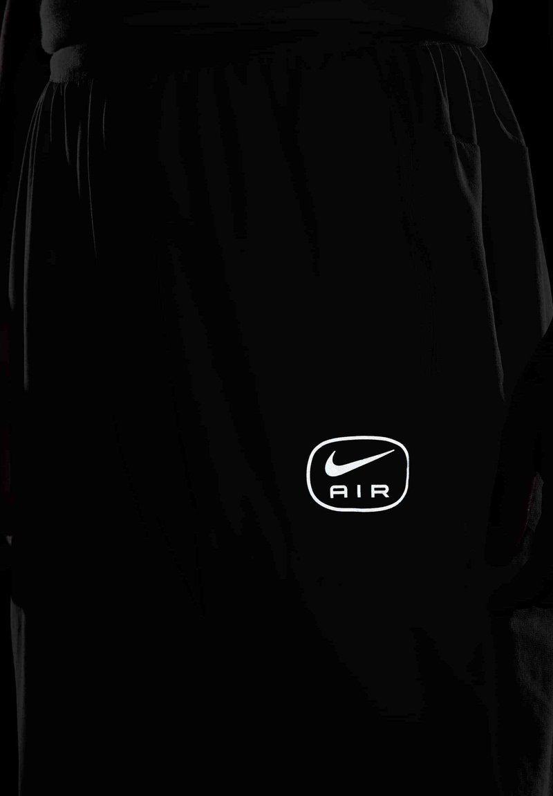 Shorts de sport noirs avec un logo réfléchissant "Nike AIR" sur le bas à gauche, dotés d'une taille avec cordon de serrage et de poches latérales.