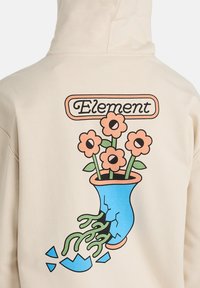 Sudadera con capucha beige con un gráfico de un jarrón azul roto que sostiene cinco flores durazno con tallos y hojas verdes, y la palabra "Element" encima.