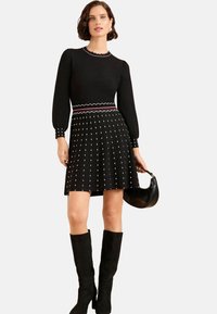 Abito nero a maglia con maniche lunghe, caratterizzato da un collo scallop, gonna con motivo a pois bianchi e una vita con accenti rosa e bianchi.