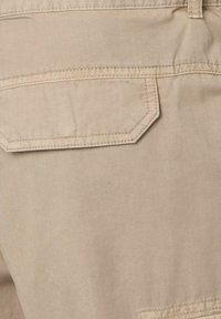 Beige stof met een gladde textuur, met een rechthoekige achterzak met een rechte klep en contrasterende stikdetails.