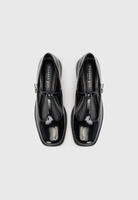 Pantofi Mary Jane din piele lacuită neagră, cu vârf pătrat, design cu bretea T și detalii cu cataramă argintie. Textură netedă cu finisaj lucios.