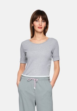 Woman with shoulder-length brown hair wearing a gray short-sleeve top and light blue pinstriped pants with a pink drawstring, hands in pockets.