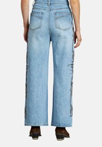 Jeans de mezclilla de un azul claro, de pierna ancha y cintura alta, con dos bolsillos traseros, que presentan un intrincado bordado negro a lo largo de las costuras laterales.