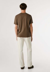 Camiseta marrón de manga corta con cuello redondo, combinada con pantalones rectos de color claro. Diseño simple, textura suave, sin patrones visibles.