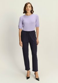 Lichtpaarse gebreide trui met korte mouwen, gecombineerd met donkere marineblauwe tapered broek met een drawstring taille en zijpiping. Zwarte hakken.