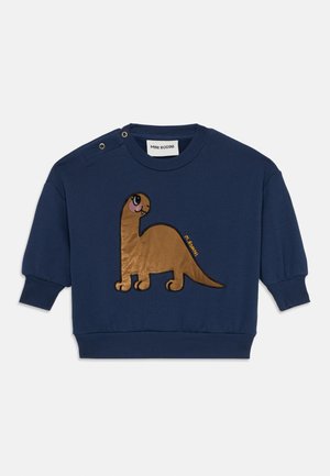 Sweatshirt marine avec une application de dinosaure marron. Présente des poignets et un col côtelés, des pressions sur les épaules, et une texture douce. Étiquette de marque visible.