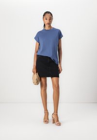 Blaues T-Shirt mit kurzen Ärmeln und Rundhalsausschnitt, kombiniert mit einem schwarzen Denim-Minirock. Die Accessoires umfassen eine beige Clutch und sandfarbene Blockabsatz-Sandalen.
