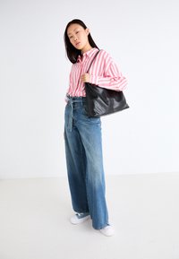 Svart läder axelväska, rosa och vita randiga skjorta med knappar, blå vida jeans. Vita sneakers fulländar looken.