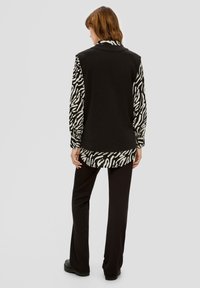 Maglietta oversize in bianco e nero con maniche lunghe a motivo zebra e retro, abbinata a pantaloni neri. Presenta un colletto e un orlo arrotondato.