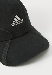 Crna kapa izrađena od teksturirane tkanine, s srebrnim izvezenim Adidas logotipom sprijeda i zakrivljenim vizirima s detaljima šivanja.