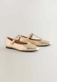 Goldene metallische Ballerinas mit Ausschnittdesign und Knöchelriemen. Glatte Textur, spitze Zehen und niedriger Absatz. Schlichte und elegante Verarbeitung.