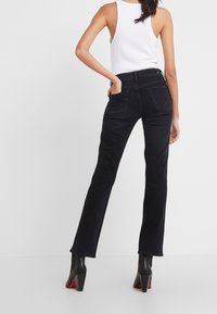 Pantalones vaqueros acampanados negros de mezcla de algodón, con bolsillos traseros y cintura de altura media. Combinados con una camiseta blanca sin mangas y botas negras de tacón.