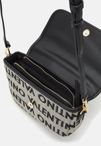 Černá a šedá kabelka přes rameno s plátěným povrchem zdobeným výrazným potištěným textem. Uvnitř dvě kapsy na zip, hardware v zlaté barvě.